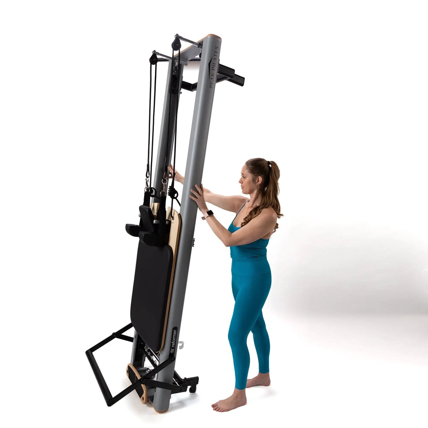 Peak Pilates Fit Reformer with Long & Short Box, gray frame and cables, user in teal on Tampa Home & Garden Store