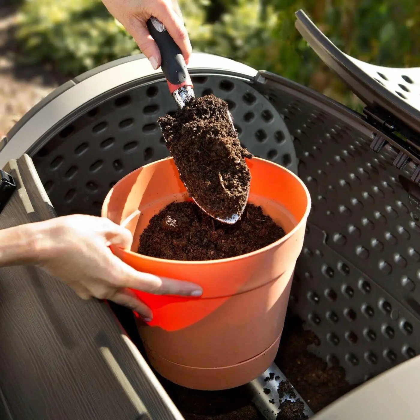100-gallon rotating compost tumbler with hand scooping dark compost into orange bucket on Tampa Home & Garden Store