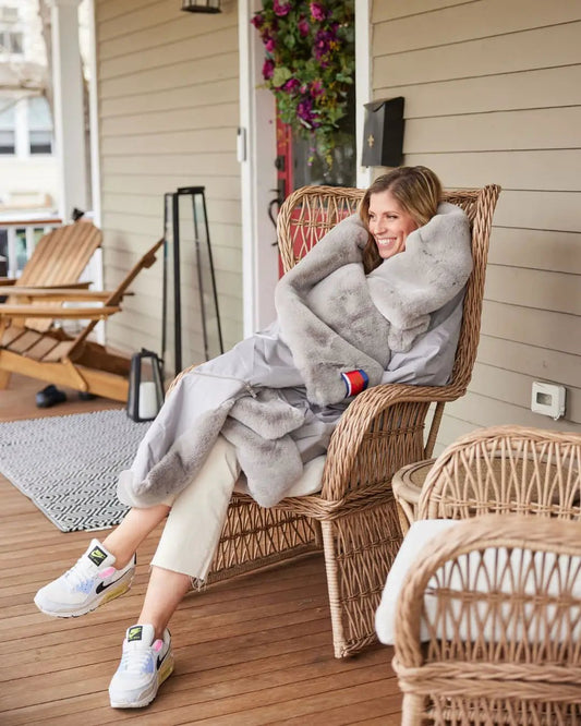 Waterproof Windproof Large Outdoor Blanket in gray plush on a porch chair with a smiling woman on Tampa Home & Garden Store