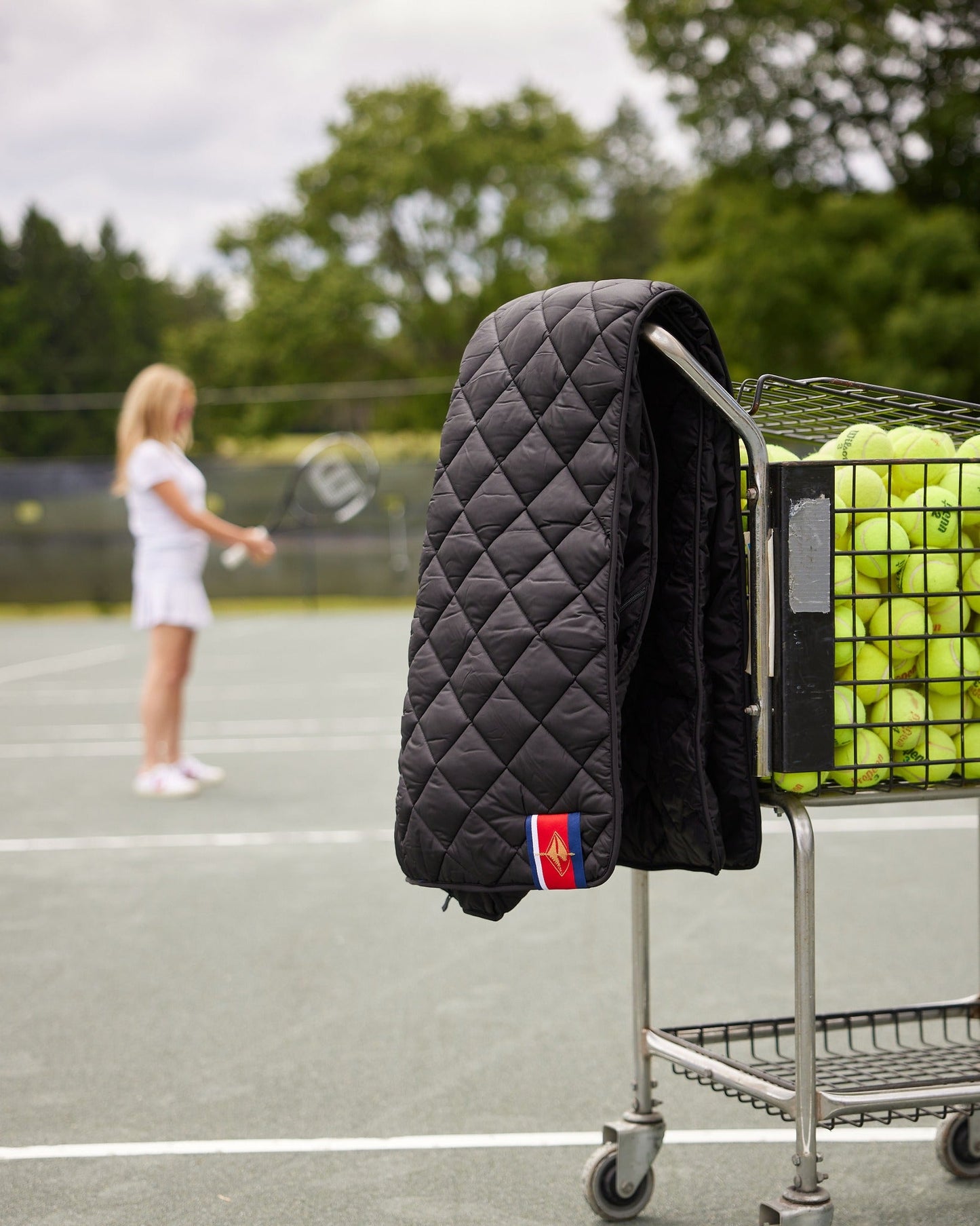 Football on Black Puffer Blanket draped over a cart with tennis balls on a sunny court on Tampa Home & Garden Store