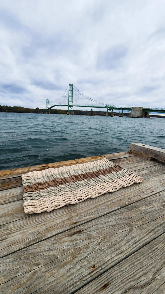 5 Stripe Lobster Rope Mat in light tan with brown stripes, braided rope texture on a dock by water on Tampa Home & Garden Store