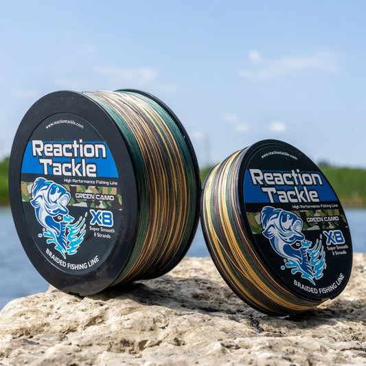 Reaction Tackle X8 braided fishing line spool in green camo, two spools on rocky shore by water on Tampa Home & Garden Store