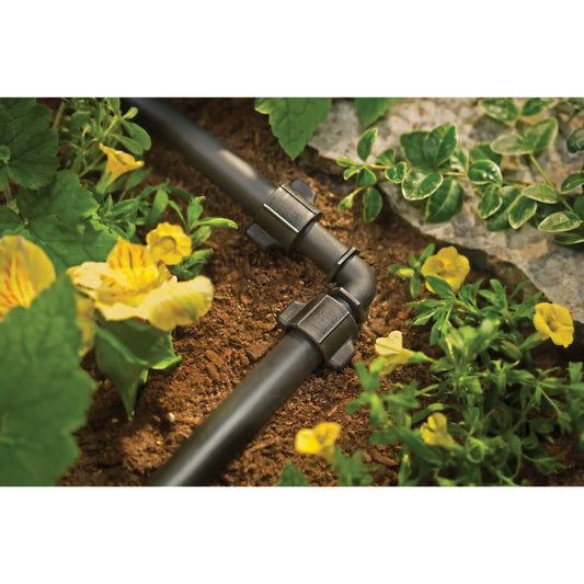 Half Inch universal drip elbow for tubing on black irrigation line amid soil and yellow flowers on Tampa Home & Garden Store