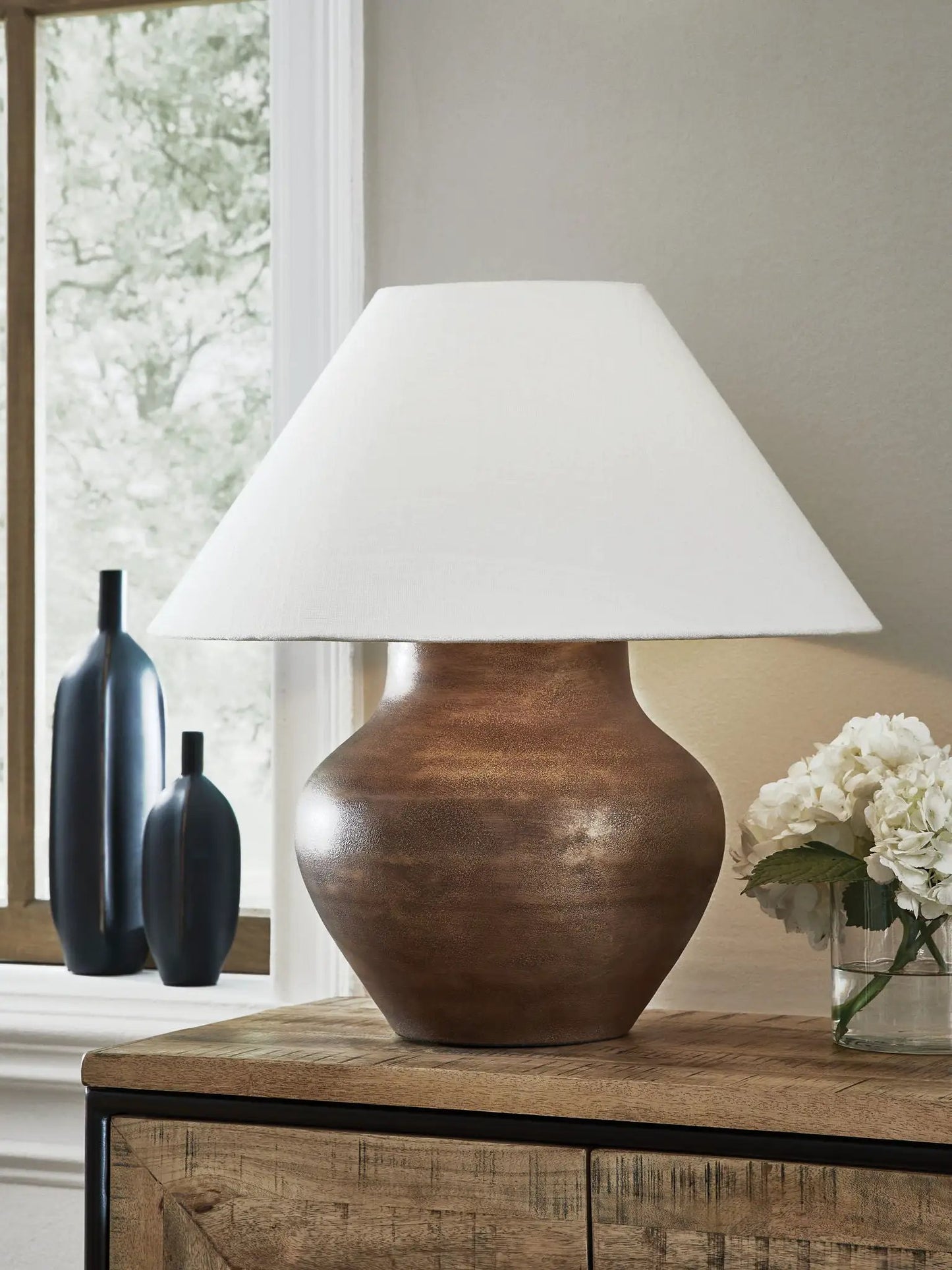 Whitham metal table lamp with antique copper finish, white linen shade, set on wood table on Tampa Home & Garden Store