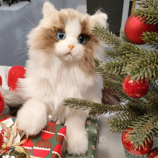 Ragdoll weighted plush stuffed animal with blue eyes and cream-brown fur beside a Christmas tree on Tampa Home & Garden Store