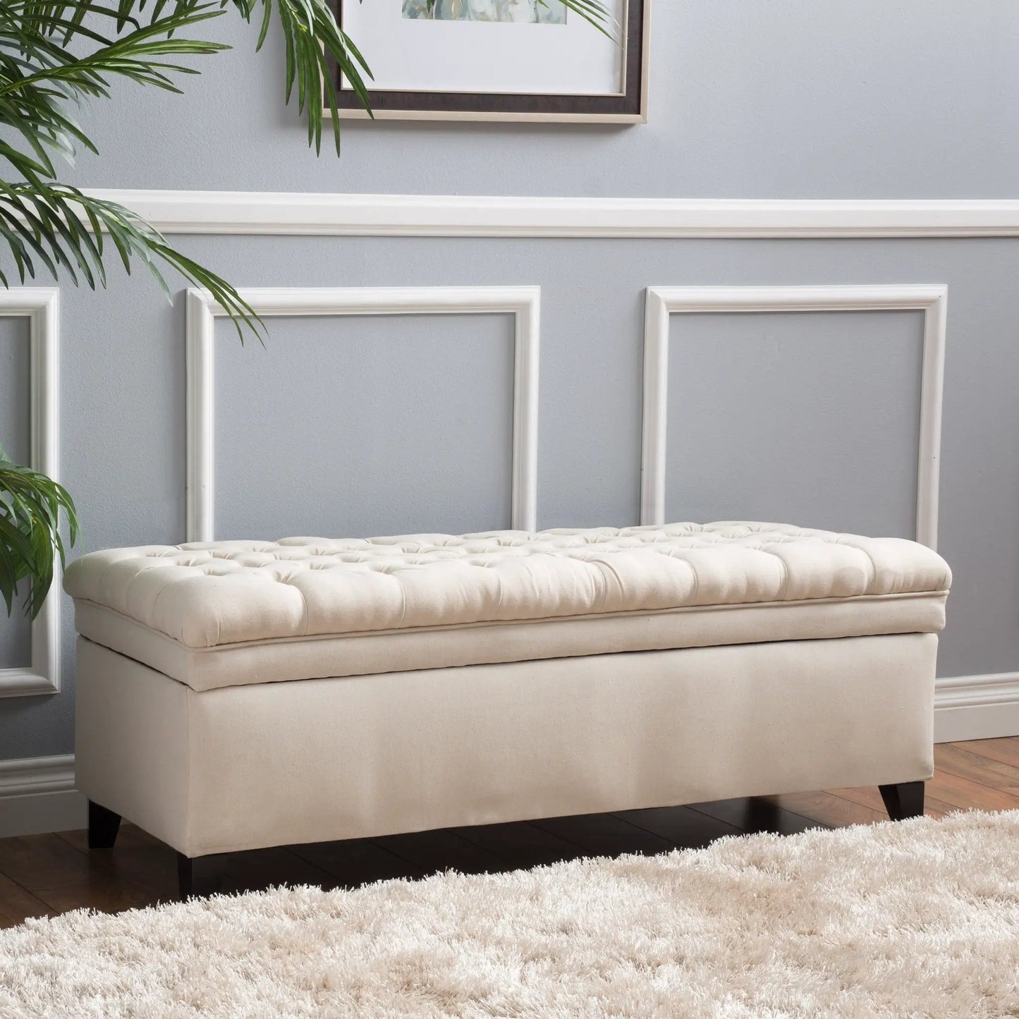 Juliana beige fabric storage ottoman with tufted lid and dark wood legs in a gray room on Tampa Home & Garden Store