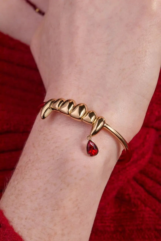 Gold-tone vampire teeth cuff bracelet by ALEX AND ANI with a red teardrop charm on wrist on Tampa Home & Garden Store