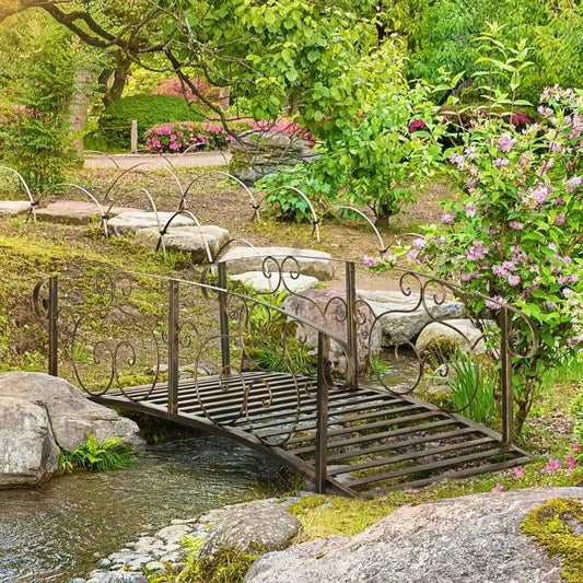 Outdoor bronze arch garden bridge with ornate rails by HomePacific over a stream on Tampa Home & Garden Store