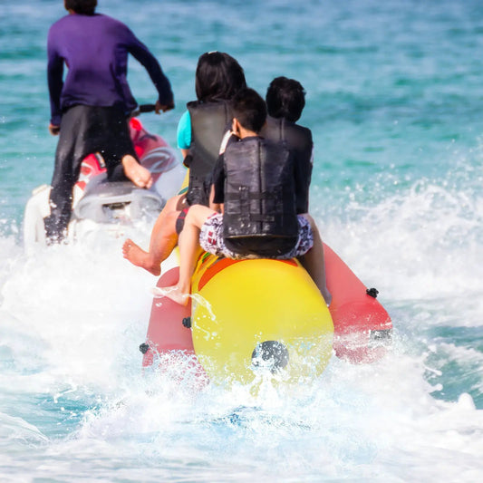 Three-person inflatable banana boat with yellow body and red ends, riders wearing life jackets on Tampa Home & Garden Store