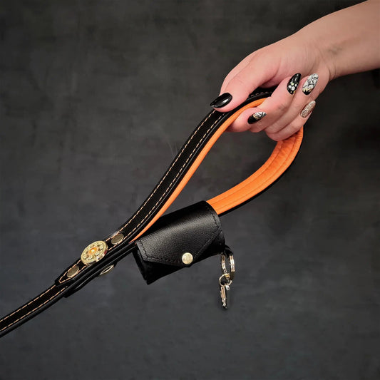 Bestia Poop Bag Holder Keychain in black leather with orange edge and brass hardware held on Tampa Home & Garden Store