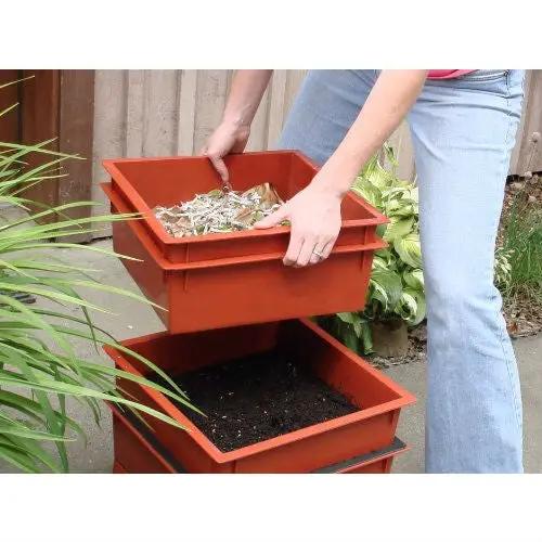 Orange plastic worm composter stackable bins with compost in top tray held by person outdoors on Tampa Home & Garden Store