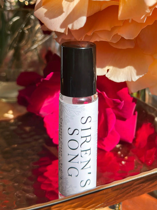 Perfume oil Siren's Song by In the Wick of Time with black cap and white label amid peach roses on Tampa Home & Garden Store