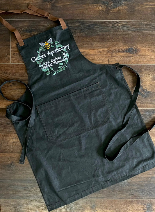 Claire's Apothecary Embroidered Apron in black denim with brown straps and front pocket on Tampa Home & Garden Store