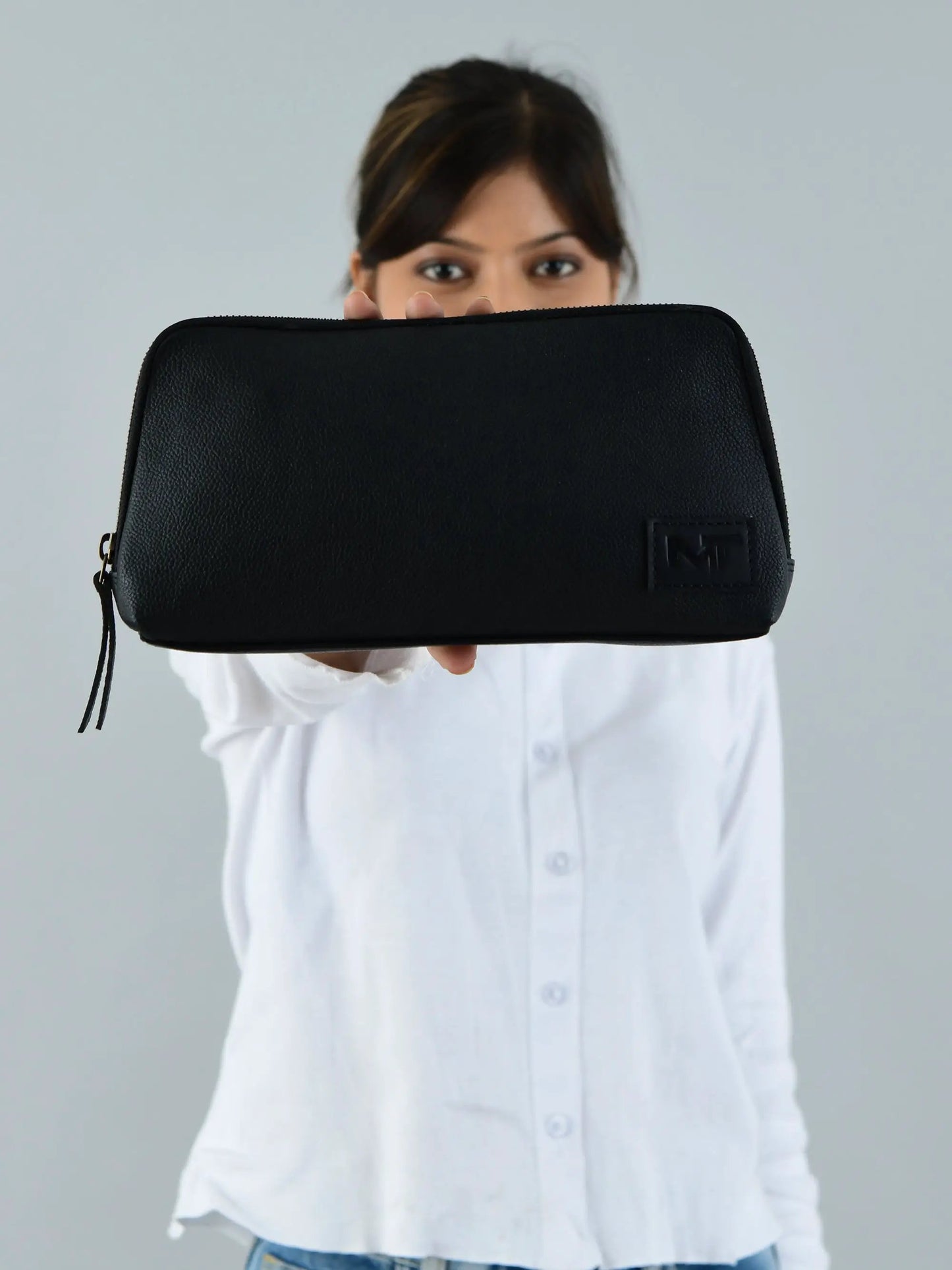 Classic black leather clutch with zipper pocket, logo patch held by a person in white shirt on Tampa Home & Garden Store