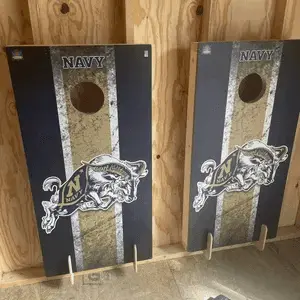 Two navy cornhole boards with gold stripe panels and a dog logo, leaning in a shed on Tampa Home & Garden Store