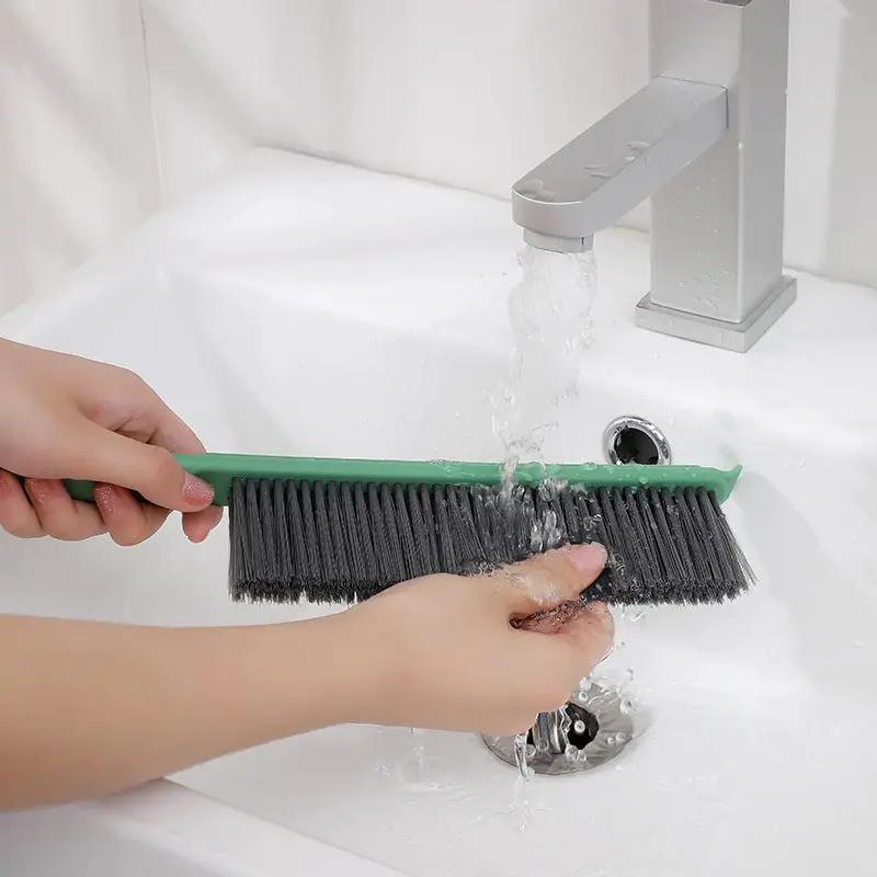 Bed brush with long green handle and black bristles being rinsed under a faucet on Tampa Home & Garden Store