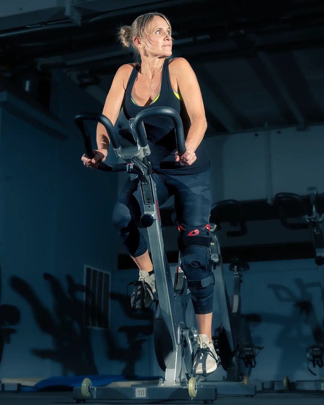 Black EVS SX01 Knee Brace with polycentric hinges worn by a rider on a stationary bike on Tampa Home & Garden Store