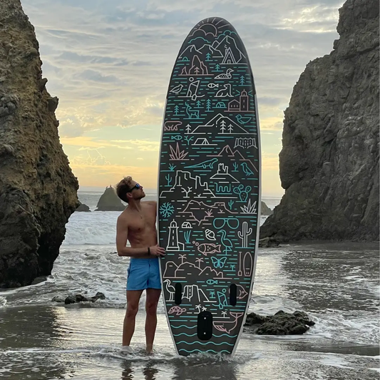 GrandSol Oasis Pack inflatable paddle board with teal artwork on beach held by a man in shorts on Tampa Home & Garden Store