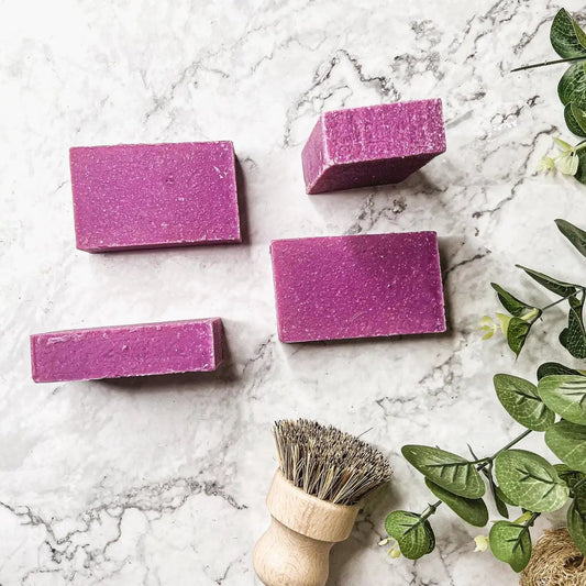 Patchouli and Raspberry soap bars with sea salt, five purple blocks on marble with a wooden brush on Tampa Home & Garden Store
