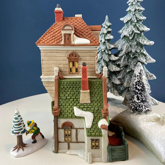 Illuminated Christmas Village Green Gate Cottage brown-tiled roof, snow, and evergreen trees on Tampa Home & Garden Store
