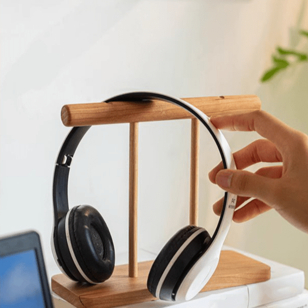 Headphones on a RusticReach wooden stand with a hand adjusting the curved rail, laptop nearby on Tampa Home & Garden Store