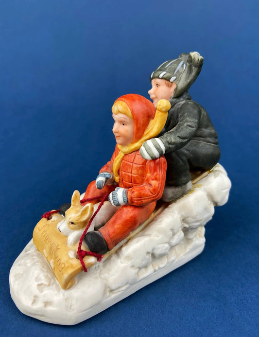 Kids and Dog on Sled porcelain figurine with orange-red coat, grey hat, snowy base on Tampa Home & Garden Store