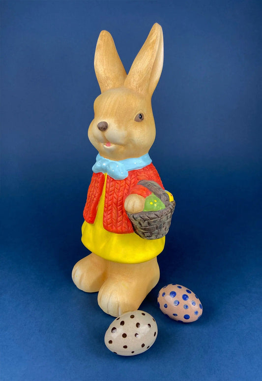 Bunny figurine carrying a basket with speckled eggs, golden-brown rabbit in blue scarf on Tampa Home & Garden Store