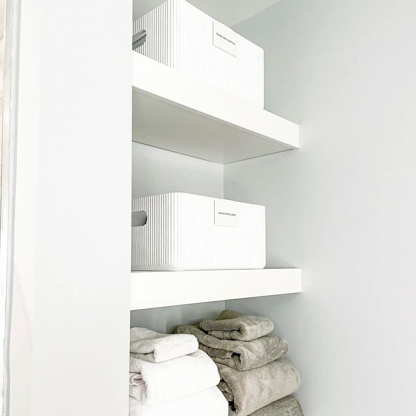 Pair of white wooden ribbed storage bins on white shelf with folded towels below on Tampa Home & Garden Store