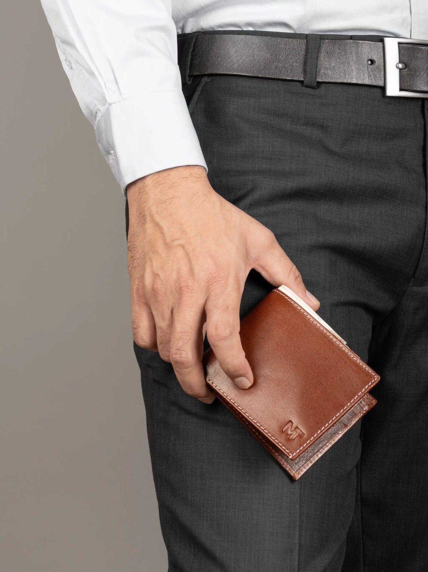 Men's Patrick Leather Bifold Wallet in brown leather with contrast white stitching embossed M logo held in a man's hand on Tampa Home & Garden Store