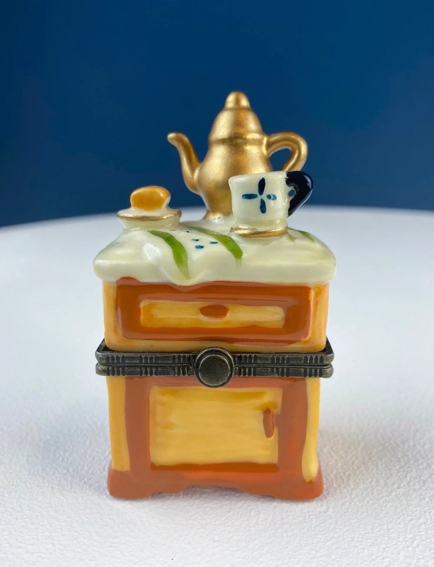 Miniature porcelain pill box dining vignette with gold teapot and blue floral cup atop a cabinet base on Tampa Home & Garden Store