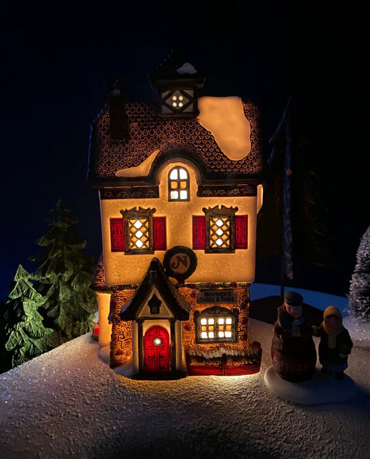 Neenee's Dolls & Toys Christmas Village House lit warmly, snow-coated roof and red shutters on Tampa Home & Garden Store