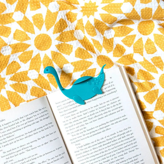 Nessie Tale bookmark turquoise blue by OTOTO DESIGN perched on an open book on Tampa Home & Garden Store