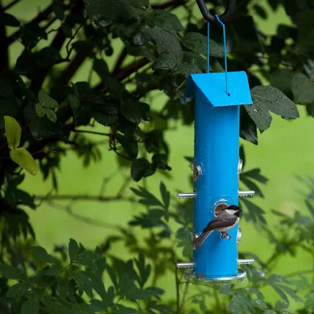 Blue 6-Perch Metal Tube Bird Feeder hanging from a hook with a small bird amid green foliage on Tampa Home & Garden Store