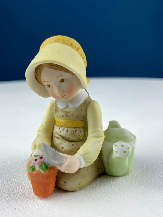 Porcelain figurine of a little girl planting flowers, wearing a yellow hat and holding a carrot on Tampa Home & Garden Store