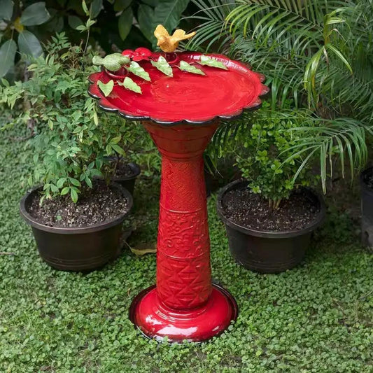 Red metal outdoor birdbath with leaf figurines in a garden setting on Tampa Home & Garden Store