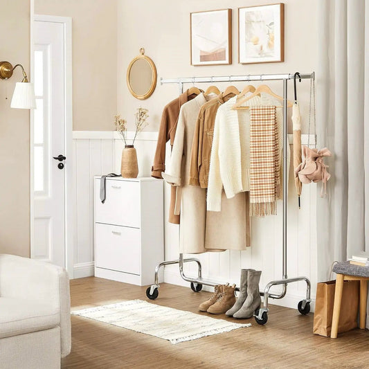 Heavy Duty Chrome Metal Tube Clothes Rack on Wheels with hanging garments in a neutral bedroom on Tampa Home & Garden Store