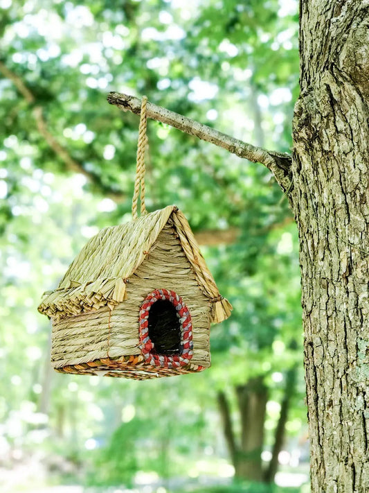 Seagrass and sari handcrafted birdhouse hanging from a tree branch with natural woven texture and red-trim entrance on Tampa Home & Garden Store