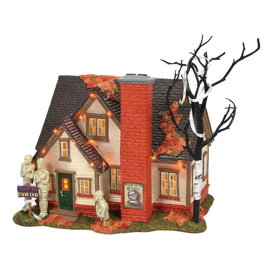 Snow Village Halloween Mummy House with lit windows, brick chimney, leaves, and a bare tree on Tampa Home & Garden Store