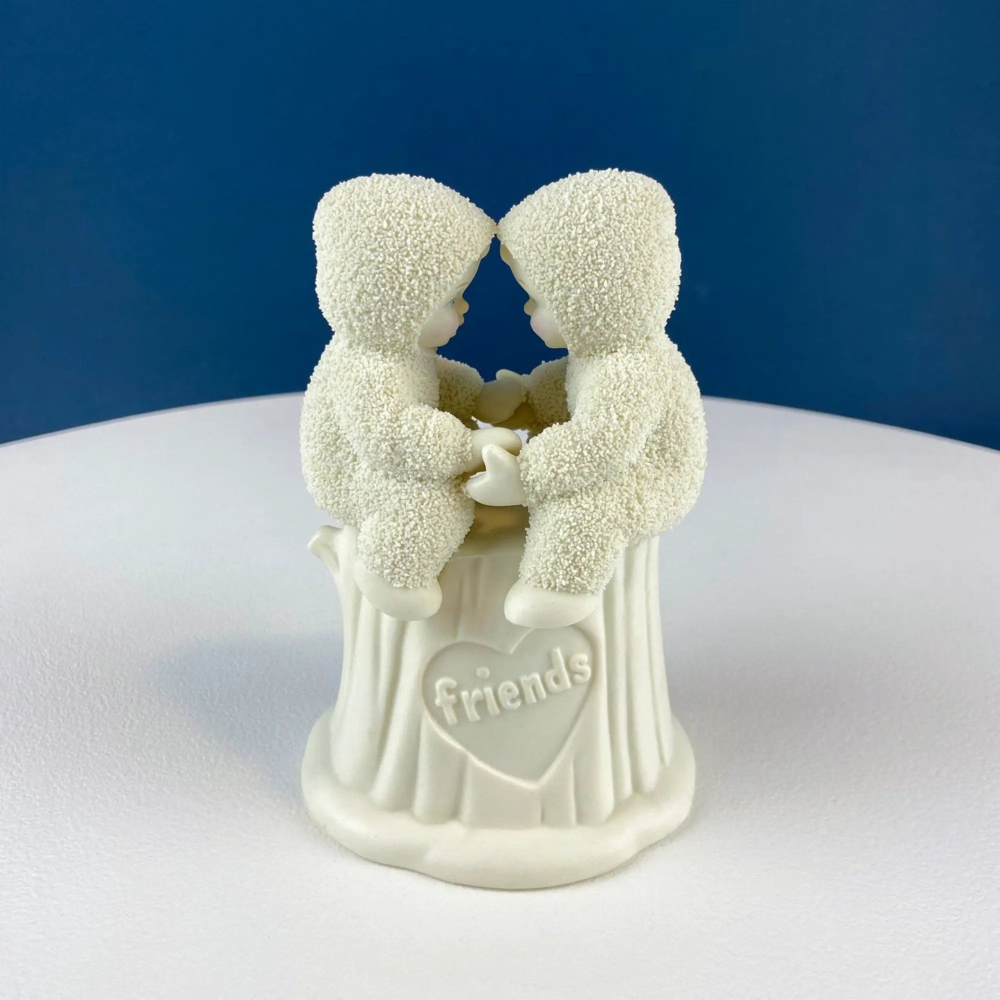 Two Snowbabies figurines facing each other in white outfits, holding hands on a pedestal on Tampa Home & Garden Store