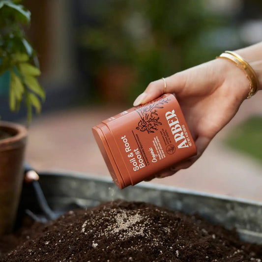 Organic Soil & Root Boost with Mycorrhizae in an orange bottle held over soil for houseplants on Tampa Home & Garden Store