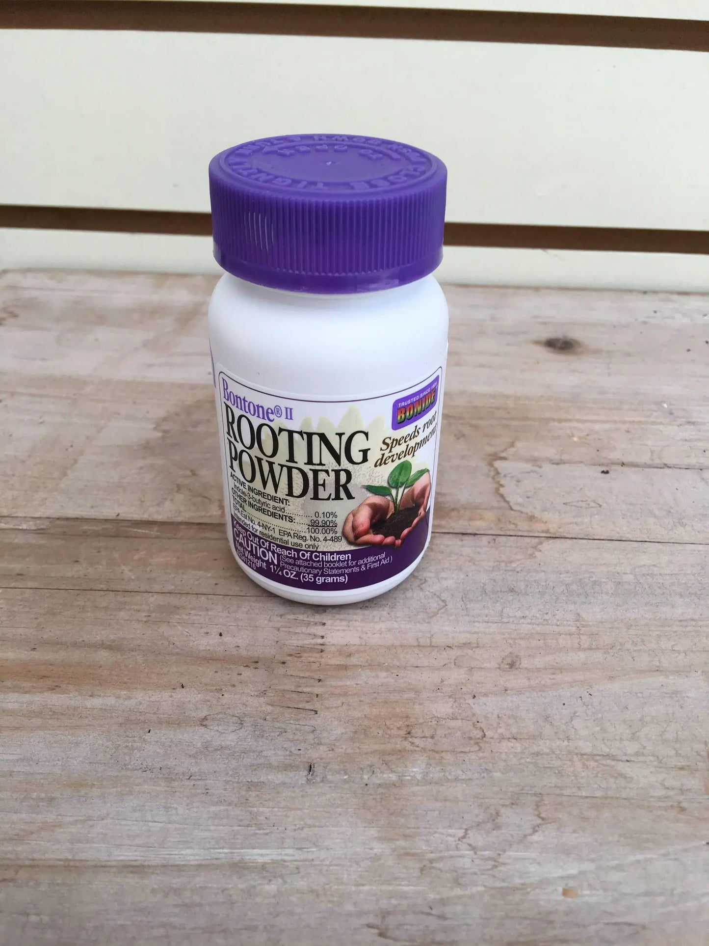 Rooting powder bottle with purple cap and Bonide label on white bottle resting on wood on Tampa Home & Garden Store
