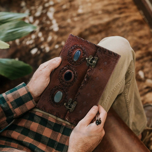 Vintage leather journal with three blue stone accents held by plaid-clad hand on Tampa Home & Garden Store