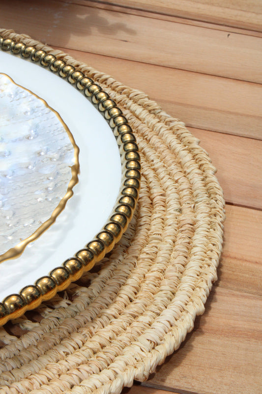 Natural raffia placemat with handwoven texture and gold bead rim beneath a white plate on wood on Tampa Home & Garden Store