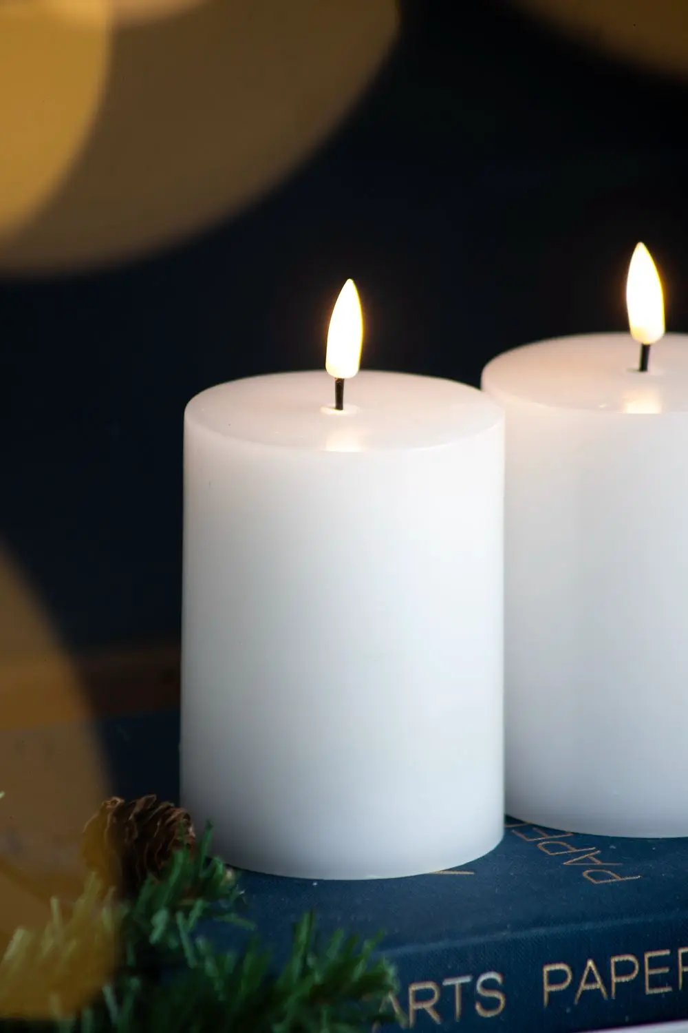 LED candles with wick and remote timer, white pillar set of 2, lit on blue book with greenery on Tampa Home & Garden Store