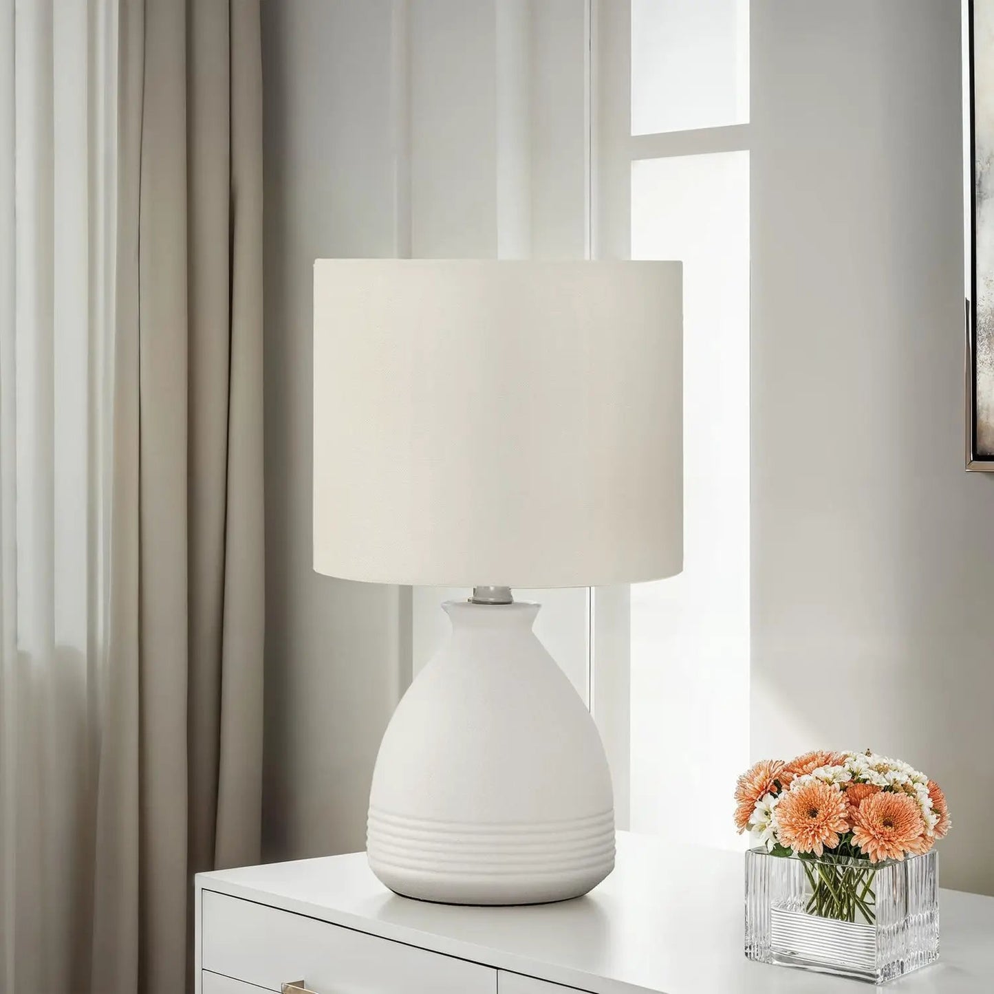Modern cream table lamp with textured ceramic base on a white dresser beside orange flowers on Tampa Home & Garden Store