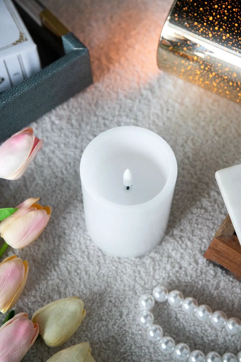 White LED candle with remote timer sits on a carpet beside pink tulips and a pearl necklace on Tampa Home & Garden Store