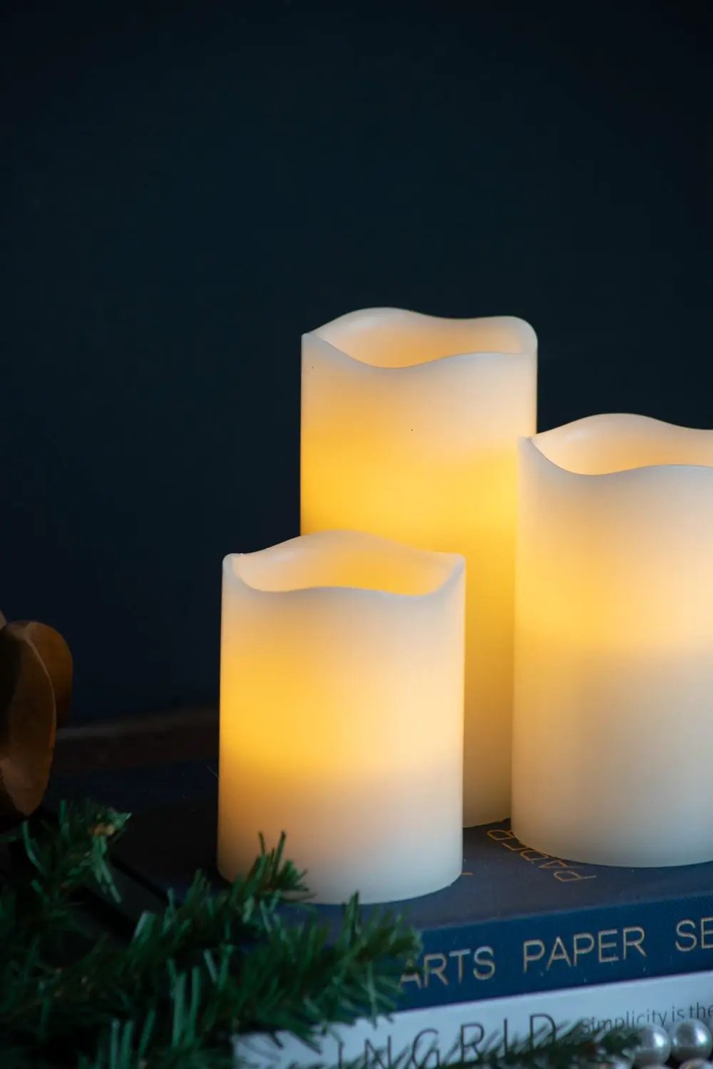 LED Candles With Remote Timer Set of 3 Ivory wavy-top pillars emitting warm glow beside books on Tampa Home & Garden Store