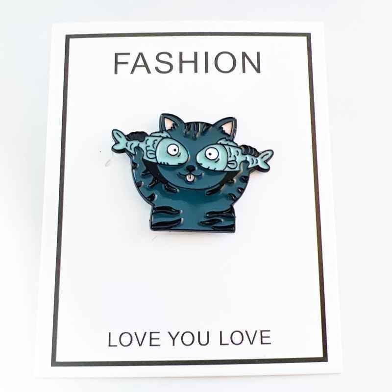 Cat enamel pin by Shaketea with goofy teal blue cat and fish arms on white card on Tampa Home & Garden Store