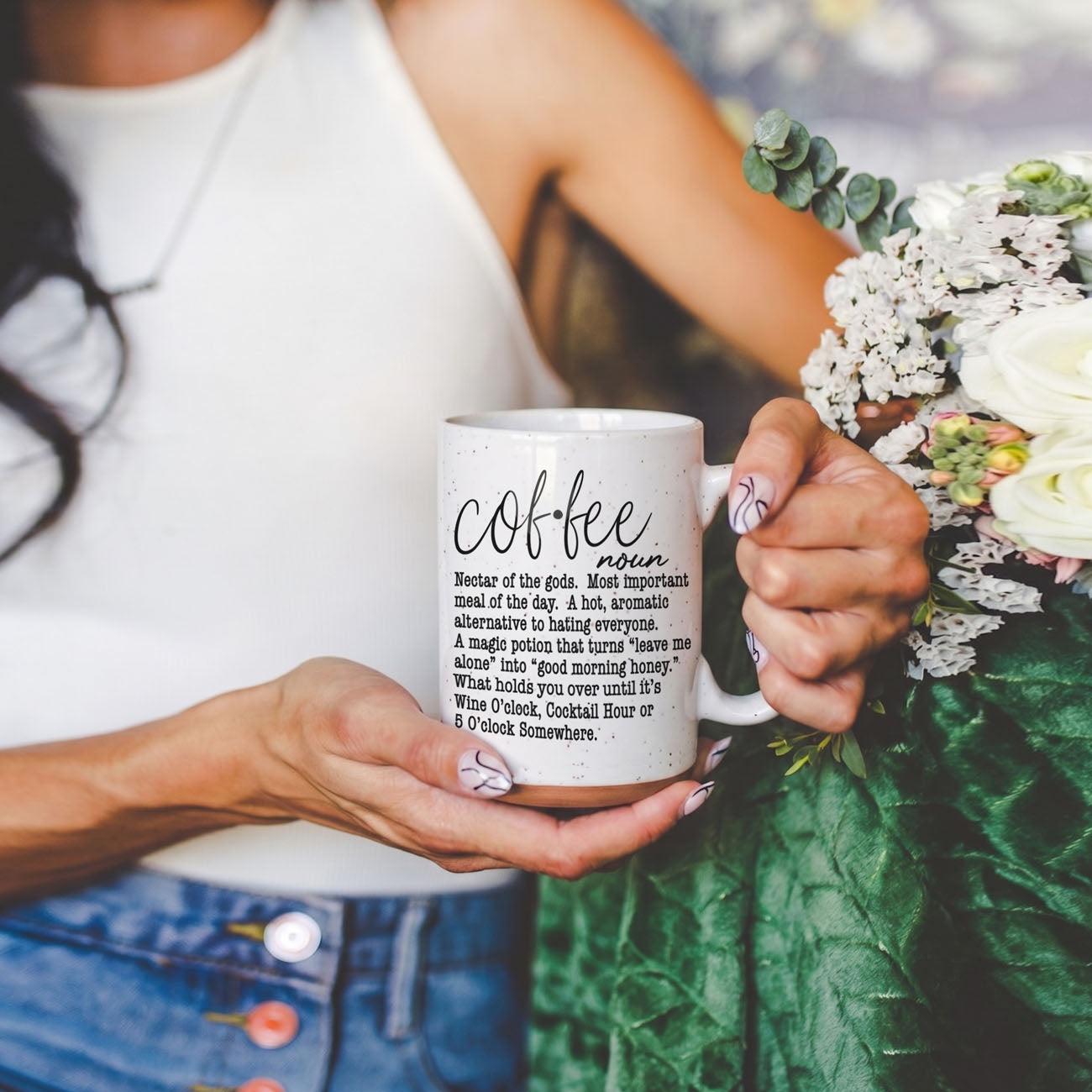 Coffee Def 16oz mug, white speckled ceramic, held by a woman beside a bouquet on Tampa Home & Garden Store