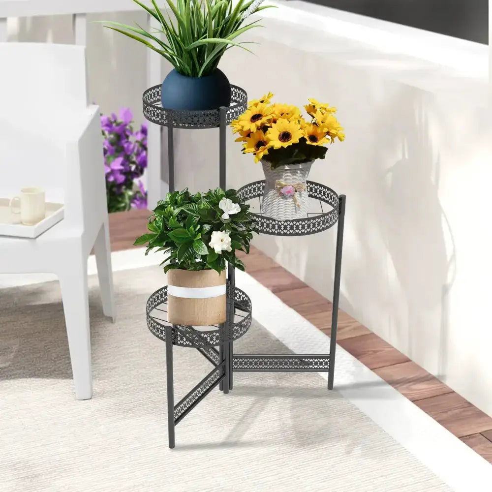 Tiered black metal plant stand with lattice; three shelves hold blue pot plant and sunflowers on Tampa Home & Garden Store